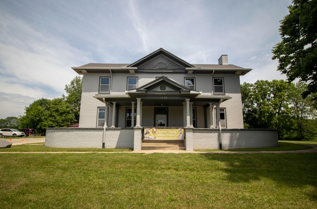 A large grey house with dark grey shutters with a green lawn out front under a blue sky