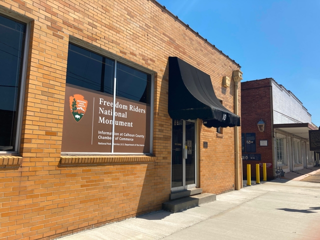 street view of a yellow brick bus depot, with a black awning and NPS sign, and an alley entrance.