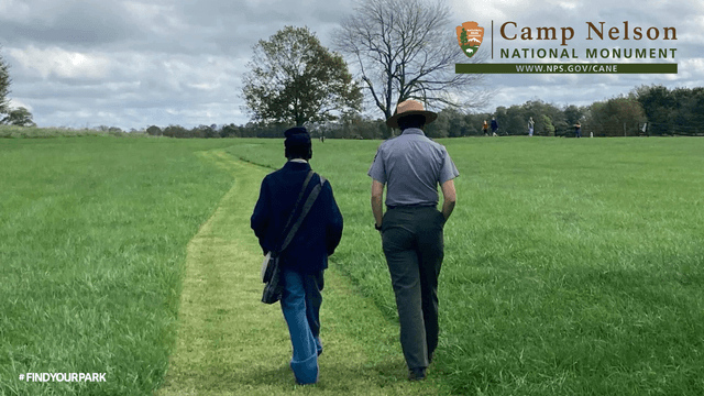 A living historian wearing a US Army Civil War uniform and park ranger walk on a mowed path.