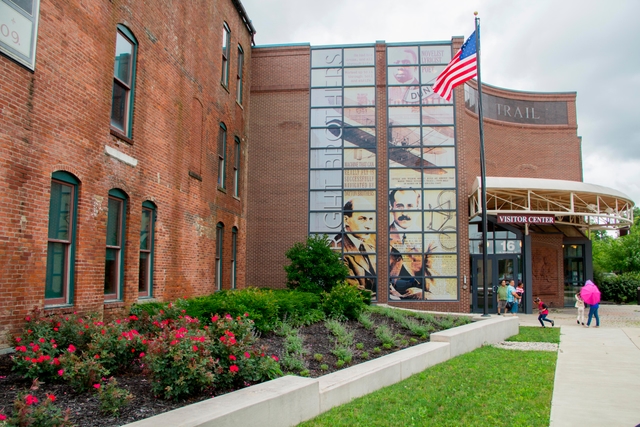 A three-story brick building with tall green windows and a tall photo mural on the glass wall