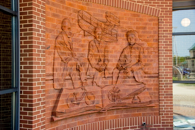 A brick wall with artwork of three men and an airplane etched out of the brick.