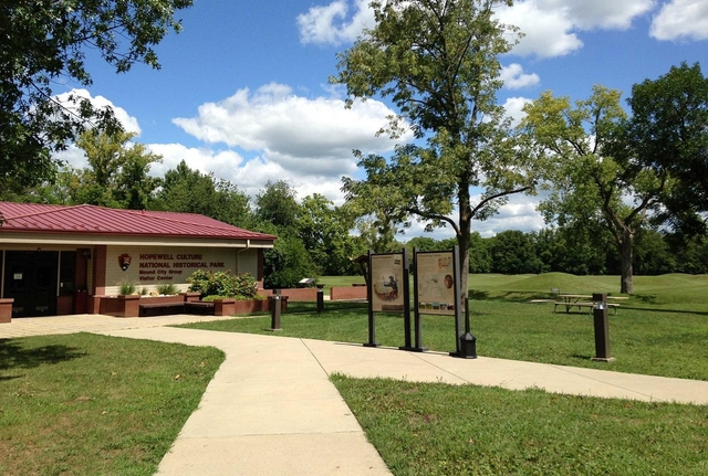 A tan building with a red-peaked roof surrounded by green grass and tan sidewalks