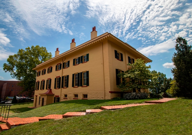 A yellow two-story brick building with tall windows and green shutters on them