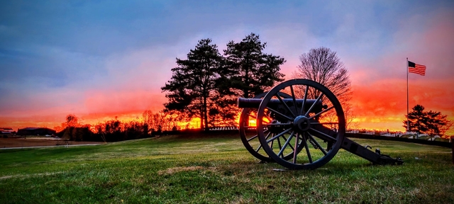 A orange sunset over the white granite headstones in the national cemetery with silhouetted cannon.