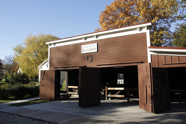 A low brown barn-like building with three large doorways has a large horseshoe on its facade.