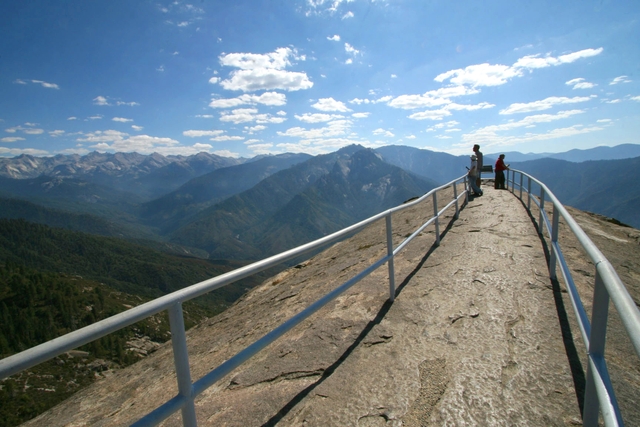 A guardrail encircles people along a narrow walkway with wide views