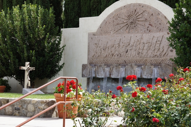 Red roses bloom near a fountain and grave marker