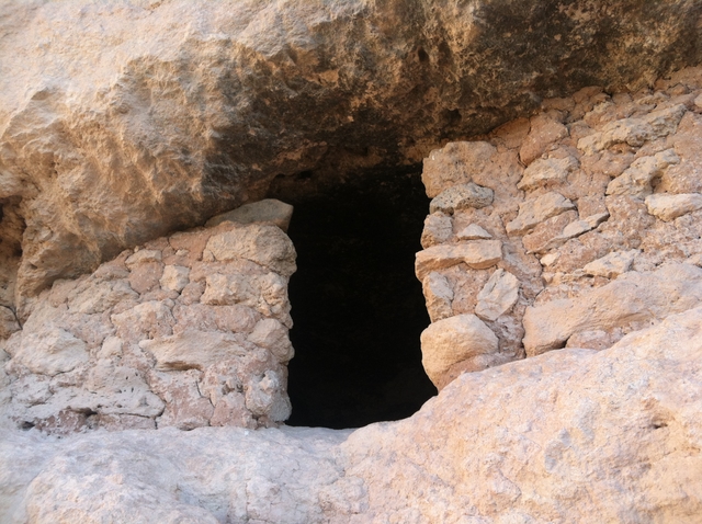 Two masonry walls with a dark doorway in a short cliff ledge.