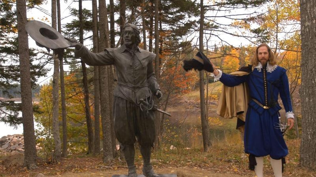 A bronze sculpture of Pierre Dugua with a reenactor standing nearby.