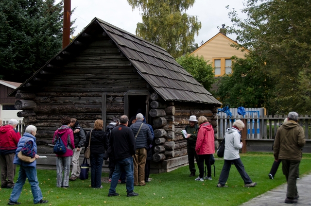 Group of people gathered around a log cabin with a ranger