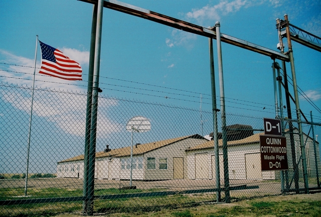 A brown building behind a tall fence with warning signs