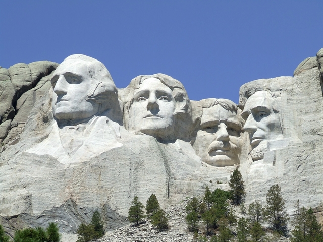 Closeup photo of Mount Rushmore under a bright blue sky.