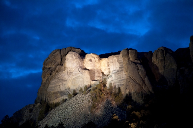 Mount Rushmore illuminated under a darkening evening sky.