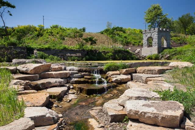 Water tumbles down layers of rock with an old stone spring house in the background.