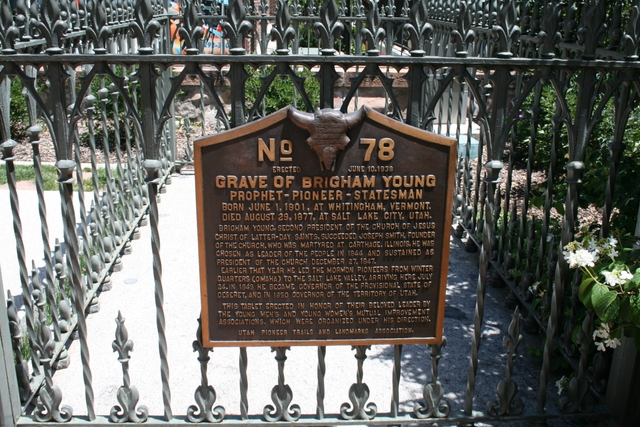 A bronze plaque with description on a metal fence surrounding Brigham Young's grave.