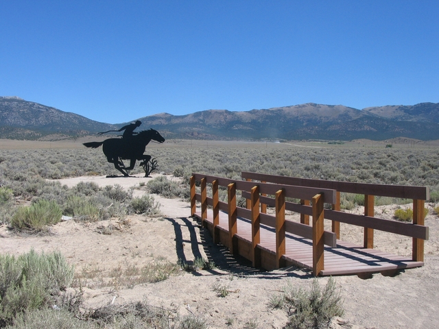 A footbridge leads to a dark steel silhouette of a Pony Express rider.