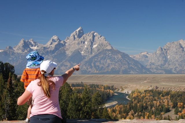 Mother in pink shirt, child in orange shirt, the Snake River below and the Teton Range beyond.