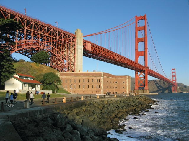 Fort Point with visitors approaching on road in front and Golden Gate Bridge above.