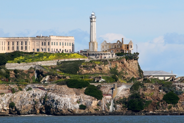 Closeup shot of Alcatraz Island showing lighthouse and prison with yellow flowers on slope in front.