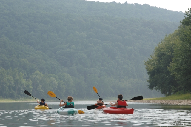 Four youngsters paddle kayaks on calm waters of the Susquehanna River