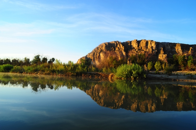 A desert river with a tree lined bank in the background.