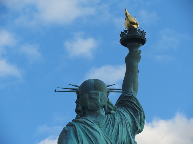 Shoulders, head, and raised right arm of the Statue of Liberty from behind the statue.