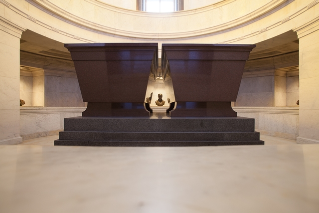 Two red stone sarcophagi are in a crypt. A bust of General Sherman can be seen in the distance.