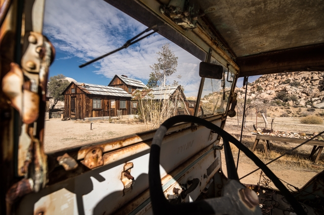 an historic wood house seen through the missing windshield of an old, rusty vehicle