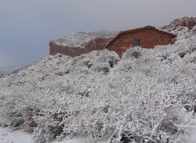 A red-orange sandstone cabin surrounded by white snow.