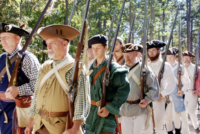 Militia reenactors march with weapons on their shoulders as they prepare to demonstrate them.