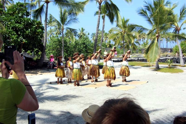 Hula dancers raise their arms to the sky in the sandy Royal Grounds.