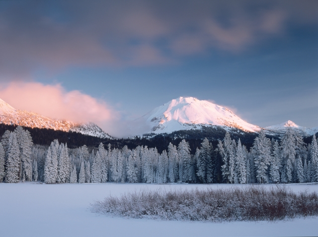 A frozen lake below snow-covered trees and peak