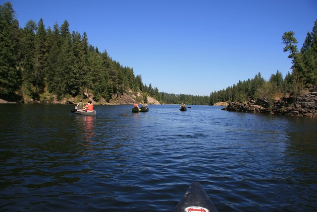 People canoeing down Lake Roosevelt on a day with blue skies.