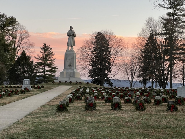 graves with wreaths leaning against the stone. tall soldier monument with pink orange sunset