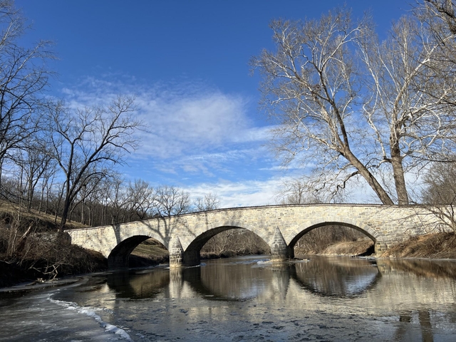 Antietam Creek flows under a three arch stone bridge blue sky