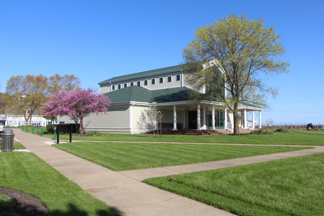 A tan building with a 2-story center window, porch and columns, surrounded by trees and a lawn