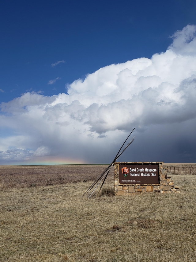 The cloud mass of a summer thunderstorm looms in the distance beyond the park entrance sign