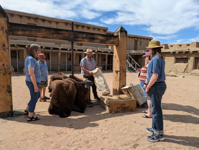 A group of visitors stand around a large wooden apparatus in a plaza courtyard.