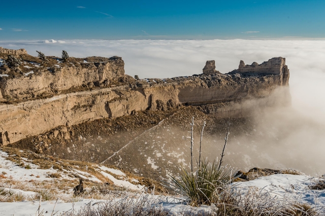 A unique rock formation is seen above a layer of clouds.