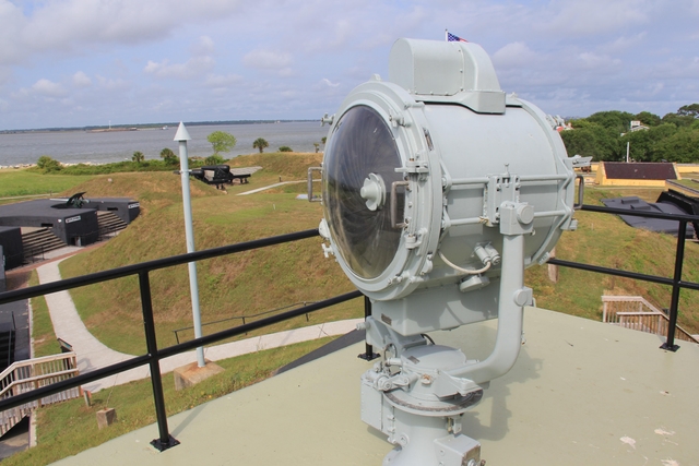 Center of image is round metal and glass signal light with grassy hills hills in background