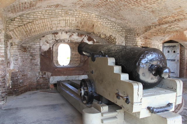 Civil War cannon sitting on carriage pointing towards firing hole in brick wall