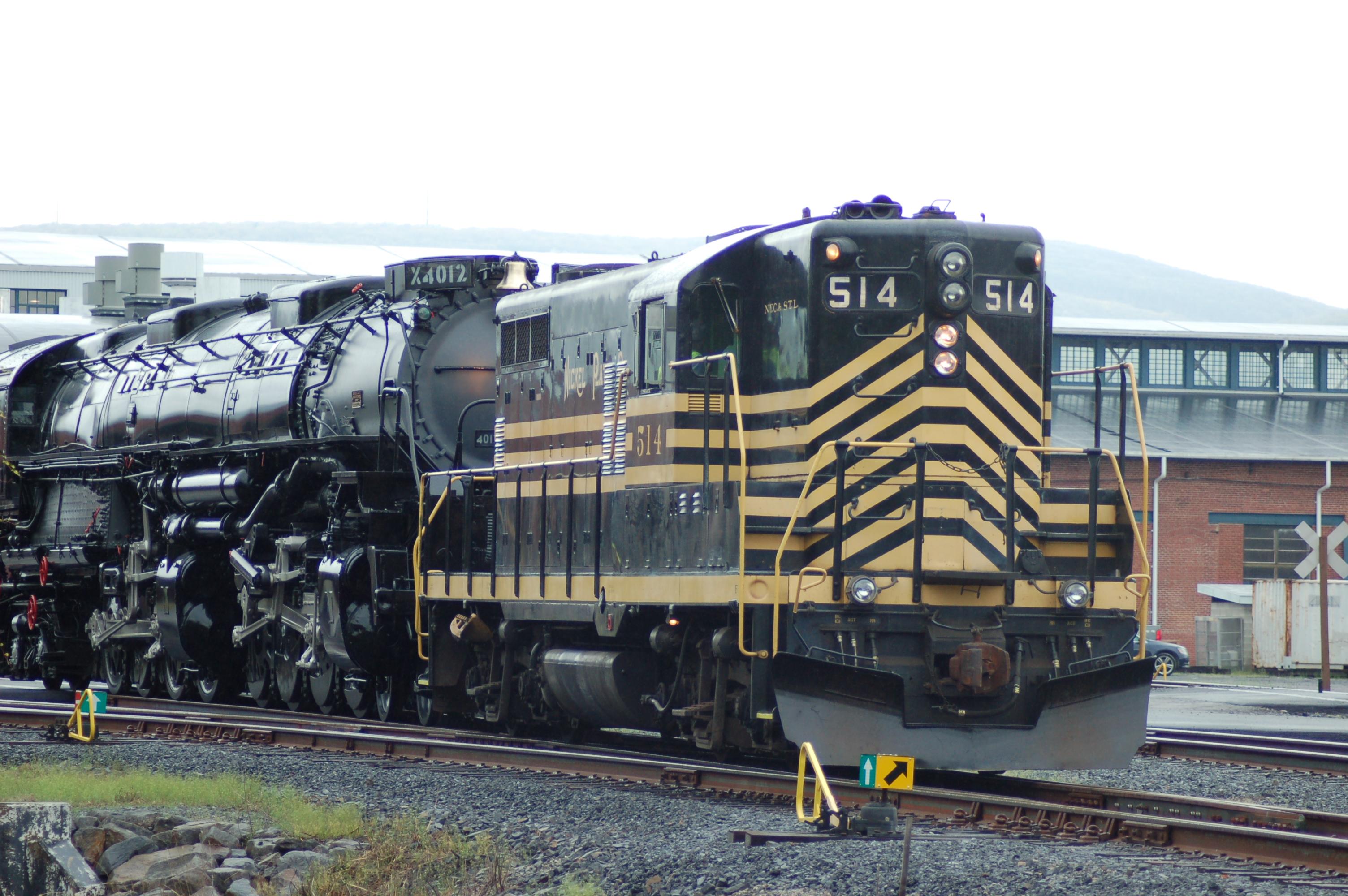 black train with yellow horizontal stripes and the number 514 pulling a larger black train on tracks