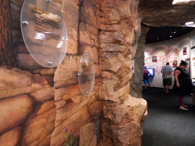 A wall mural showing red-colored rock transitions into a room with a large cave map on the wall.