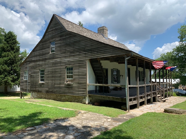 Frame house made of wood with U.S. and French flags flying on front porch.