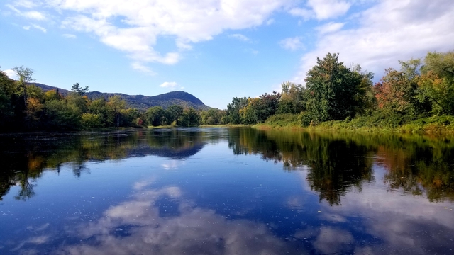 Mirror reflection of Lunksoos Mountain and trees within the water of the river.