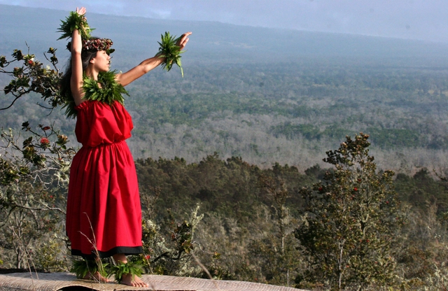 A hula dancer in a red dress above a forested area