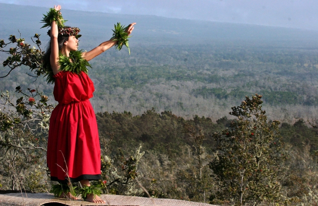 A hula dancer in a red dress above a forested area