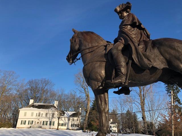 White georgian/colonial building with statue of officer on horse in foreground