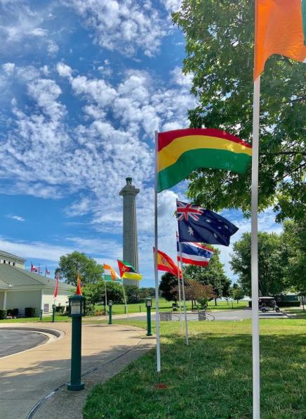 9-3'x5' international flags line sidewalk that leads to a white building with green roof. Tall stone