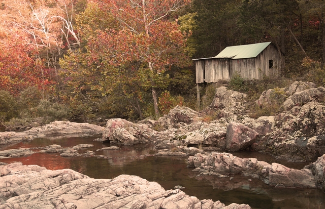 fall colors on leaves of trees surrounding a creek with an old wooden mill on the right